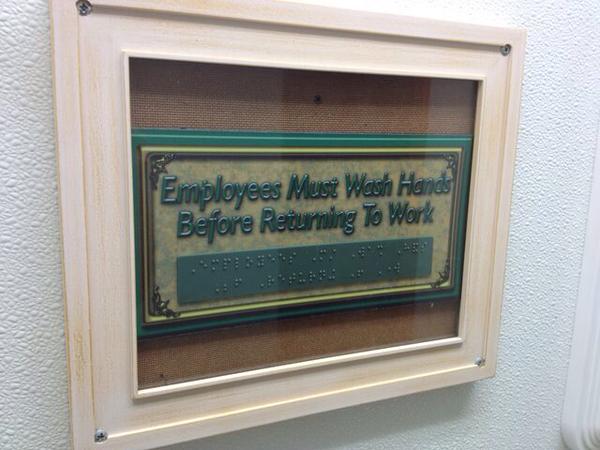A print and braille sign saying, 'Employees must wash hands before returning to work' - BEHIND A GLASS COVER
